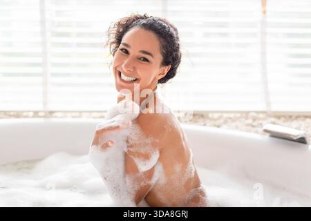 Smiling Woman Relaxing in a Bubble Bath at Home During a Calm Afternoon Stock Photo