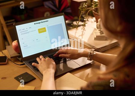 Caucasian young adult woman typing on laptop using AI image generator software at wooden desk, hands on keyboard, digital workspace with office supplies and documents visible Stock Photo