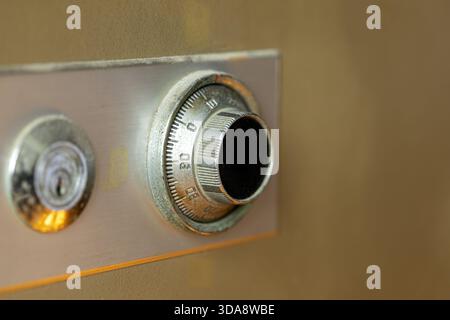 Close-up of an old metal safe combination dial and key lock on a slightly rusted beige safe door, showing wear and texture with a shallow depth of fie Stock Photo