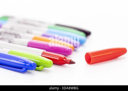 A close-up view of several colorful markers arranged in a row on a white surface, with the red marker uncapped and its top tip visible alongside the d Stock Photo