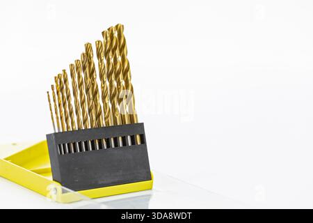 A set of gold-colored drill bits arranged in ascending size order is displayed upright in a yellow plastic case on a white background, highlighting pr Stock Photo
