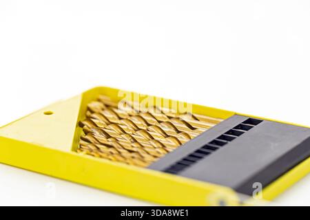 A collection of gold-toned metal drill bits neatly organized in a bright yellow plastic case with a black holder section. The drill bits are arranged Stock Photo