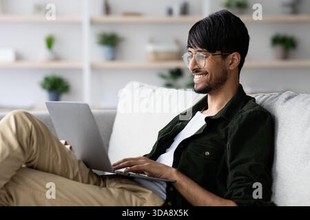 Young Man Working on Laptop at Home While Smiling and Enjoying His Free Time Stock Photo