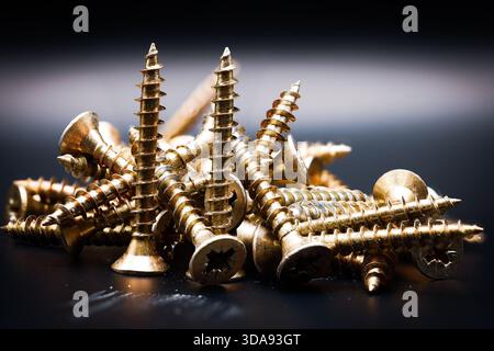 Close-up of a pile of golden metal screws on a dark background. Stock Photo