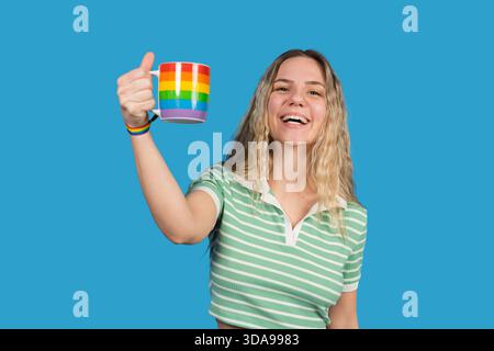 Happy woman smiling, holding a rainbow cup and giving a thumbs up Stock Photo