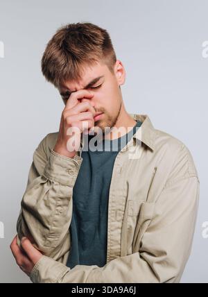 Young man in casual clothing looking stressed, touching his face. Stock Photo