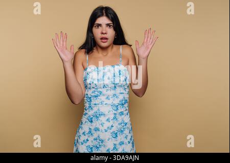 Woman in floral dress with surprised expression against beige background. Stock Photo