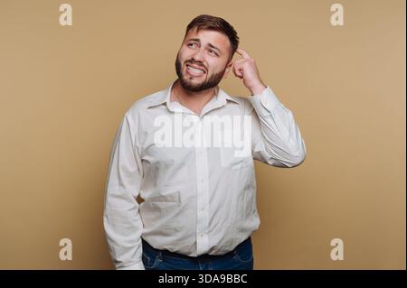 Man in white shirt scratching head with confused expression. Stock Photo