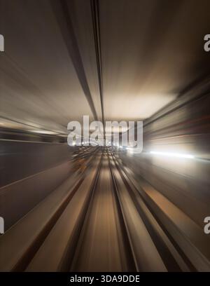 Subway train speeding through a modern underground tunnel, creating a motion blur effect reflecting speed, movement, and light Stock Photo