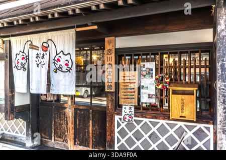 Entrance to the Miyakawa Family Museum (�m����ʷ���^) in Kiso, featuring noren curtains with a cat motif; next to it, a wooden sign displaying chopsticks from the adjoining shop. Kiso Valley, Nagano, Japan Stock Photo