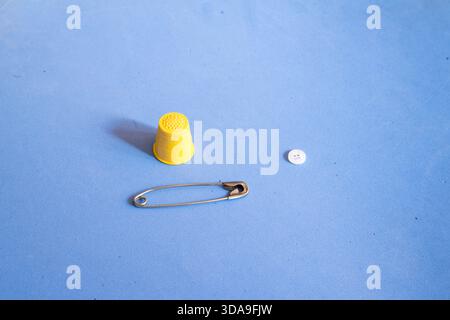 a safety pin, a thimble, and a button on a blue textured surface. Stock Photo