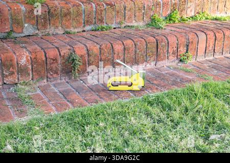 bright yellow staple gun lying on old brick steps with green grass Stock Photo