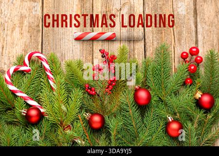 Christmas expectation. Candy cane as loading bar. Fir tree branches with red festive balls on wooden background, flat lay Stock Photo