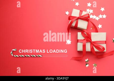Christmas expectation. Candy cane as loading bar. Gift boxes and confetti on red background, top view Stock Photo