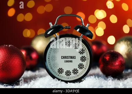 Christmas loading, holiday expectation. Alarm clock with snowflakes and festive balls against blurred lights on red background Stock Photo