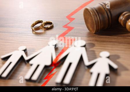 Divorce and alimony concept. Family figure with crack between wife and husband. Wedding rings and judge's gavel on table Stock Photo