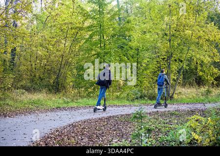 Young men are riding on the electric scooter in a park. Stock Photo
