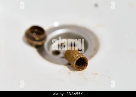 Close-up of dirty, clogged metal strainer filter mesh removed from white sink drain, showing debris and residue. Soft daylight illuminates cleaning ta Stock Photo