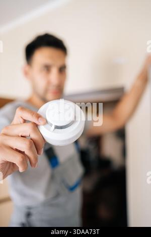 Selective focus of skilled electrician holding smoke detector while installing in residential building, prioritizing fire safety and ensuring Stock Photo