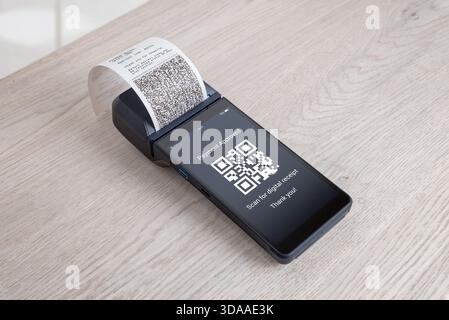odern POS terminal with printed receipt and QR code displayed on screen during approved digital payment on a clean wooden surface Stock Photo