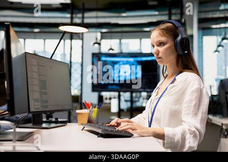 Female engineer listening music at work, adjusting deep learning algorithms parameters to automate tasks. Tech company intern wearing audio headphones working with AI insights for code optimization Stock Photo