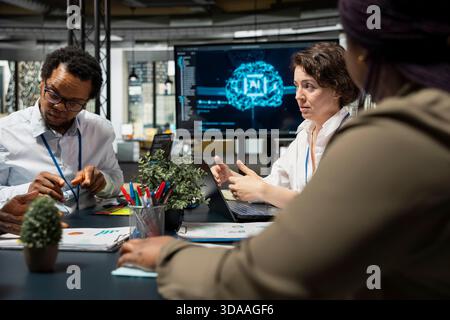 AI unicorn startup staff members discussing tech roadmap during briefing session. Computer scientists developing AI apps in office, brainstorming ways to improve company system metrics Stock Photo