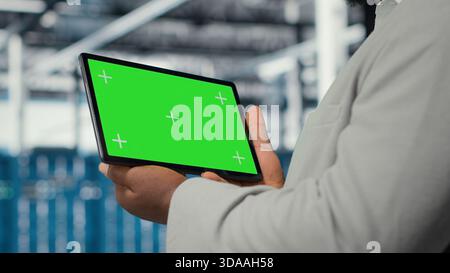 Data center IT expert uses mockup tablet, reviewing performance dashboards of equipment rigs. Server room manager overseeing systems, examining infrastructure on chroma key device, camera B closeup Stock Photo