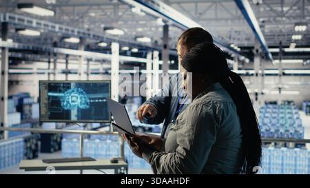 Technicians working together in server room, optimizing deep learning AI systems handling tasks. Data center coworkers doing brainstorming to adjust artificial intelligence model parameters, camera B Stock Photo