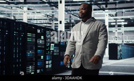 Smiling engineer walking in data center workplace with multiple rows of fully operational supercomputers. Cheerful employee overseeing server room built for digital storage systems, camera A Stock Photo