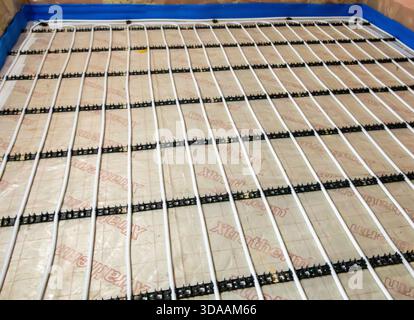 Closeup of underfloor heating system installation with plastic tubing laid over insulation and secured by black mounting rails Stock Photo