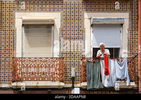 Summer, Portuguese tiled buildings, woman hanging clothes on a clothesline, balcony of tiled old building, Belem, Lisbon, Portugal Stock Photo
