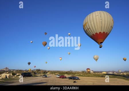 Several balloons float over a vast meadow landscape, with cars on the ground, hot air balloons, Goereme Tarihi Milli ParkIJ, Nevsehir province, Nevs Stock Photo
