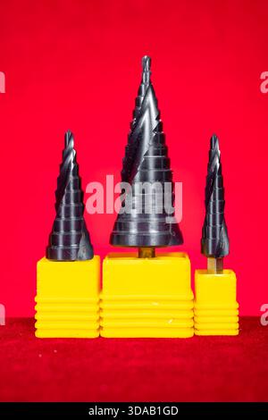 a set of conical step drill bits in various sizes on red at vertical composition Stock Photo