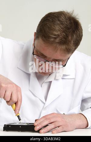 A man with a screwdriver disassembles a computer hard drive repair Stock Photo