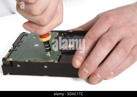 A man with a screwdriver disassembles a computer hard drive repair Stock Photo