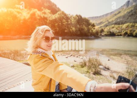 Woman, Selfie, River - Happy Woman Taking a Selfie on a Riverbank in Sunlight Stock Photo