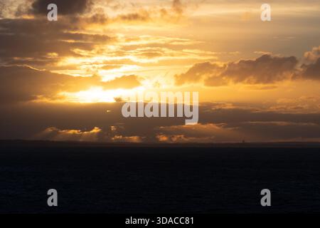 Golden sunset over Port Phillip Bay viewed from the Spirit of Tasmania ferry, with crepuscular rays piercing dramatic storm clouds above the darkened Stock Photo