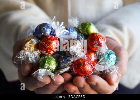 Florence, Italy, December 8, 2025. Hands holding assorted Lindt Lindor Swiss chocolates truffles. Colourfully wrapped chocolates. Stock Photo