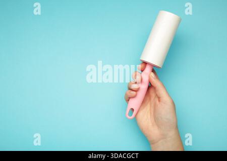 Woman holding lint roller on blue background. Space for text Stock Photo