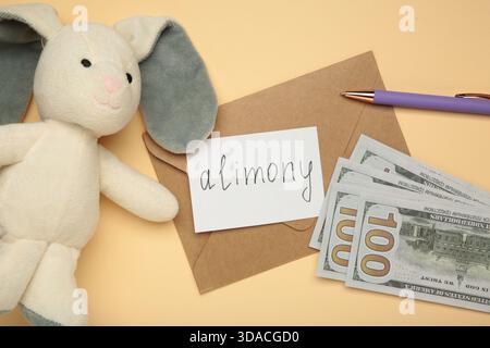Toy bunny and envelope with word Alimony and money on beige background. Top view Stock Photo