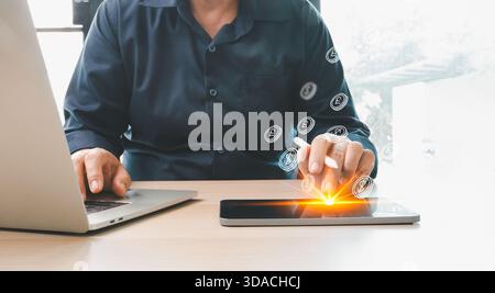 Man using laptop and digital tablet with glowing virtual currency icons, representing online payment, financial technology, digital transactions and m Stock Photo