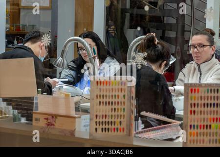Customers at a nail bar having treatments and manicures by nail technicians in a high street salon. Stock Photo