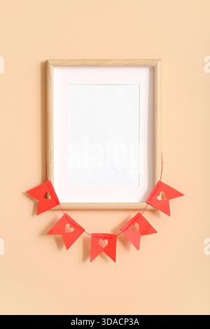 Empty frame and bunting with hearts hanging on beige wall. Valentine's Day celebration Stock Photo