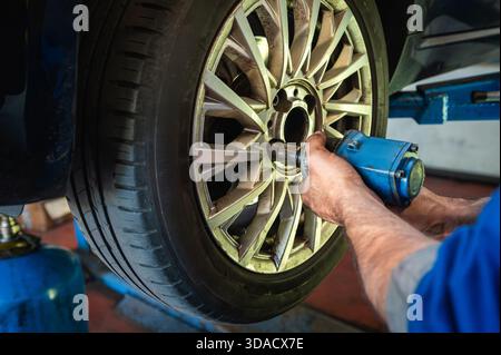 Technician using impact wrench removing lug nuts from car wheel in a garage Stock Photo
