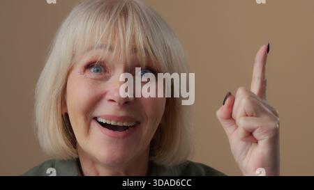 Portrait Caucasian old woman come up with idea finding answer happy smiling looking at camera in beige studio mature female senior retired granny Stock Photo