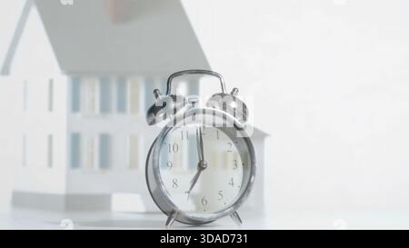 Flat design is showing silver clock sitting on white tabletop with small house, real estate theme Stock Photo