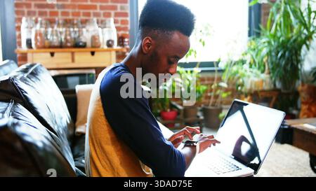Man is checking smartwatch while working on laptop on sofa in flat design loft, technology theme Stock Photo