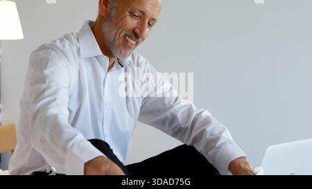 Senior man is sitting cross-legged in flat design room using laptop next to lamp for business Stock Photo
