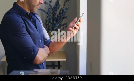 Middle-aged man is using smartphone in flat design home office, featuring business technology Stock Photo