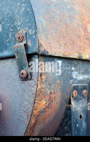 Detailed closeup of a heavily rusted metal surface featuring corroded screws, peeling layers, and rich patina colours Stock Photo